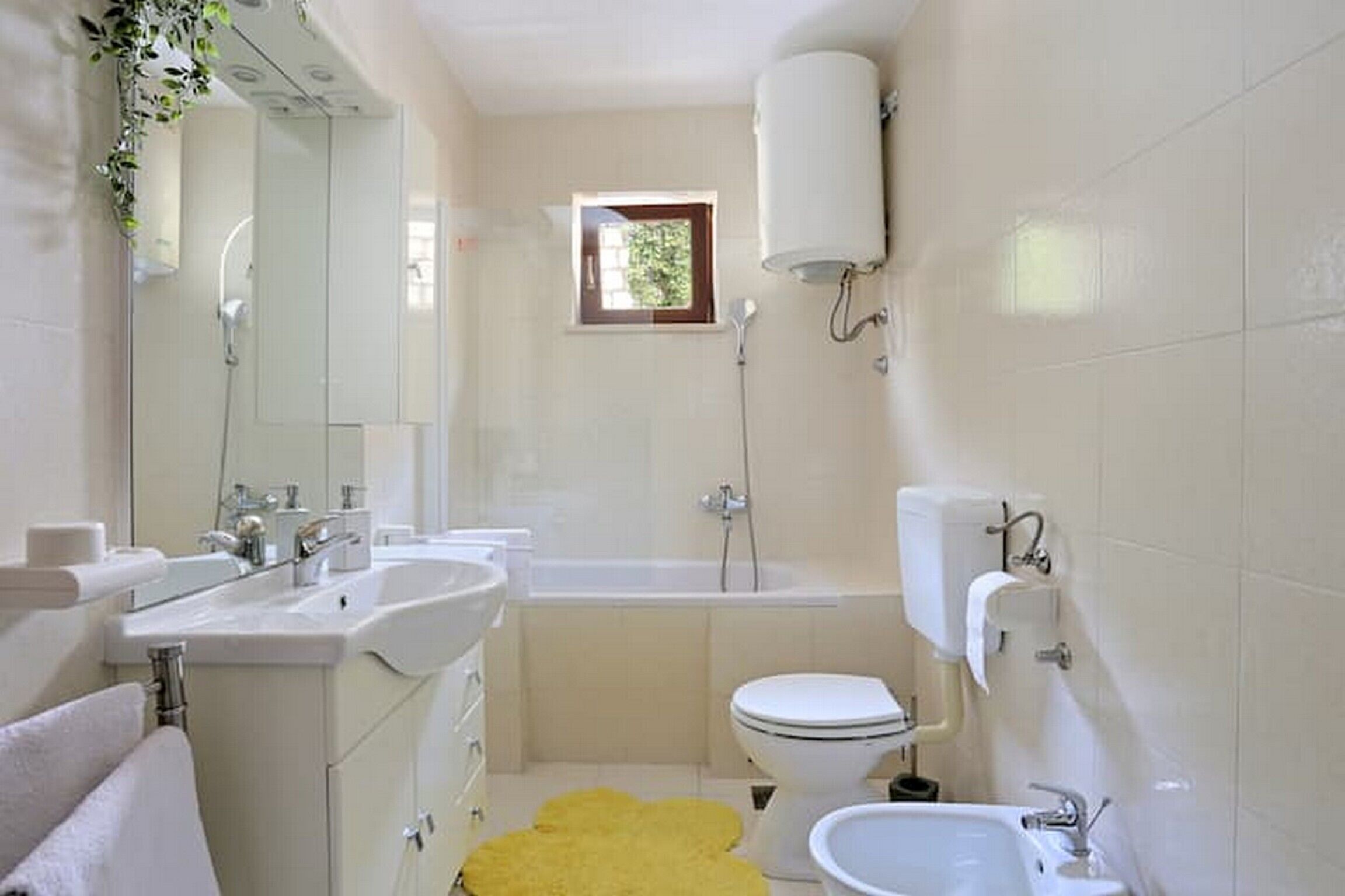 A modern bathroom with a bathtub, two sinks, a toilet, and a small window.