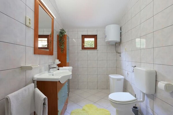 A bathroom with a sink, mirror, toilet, and a small window.