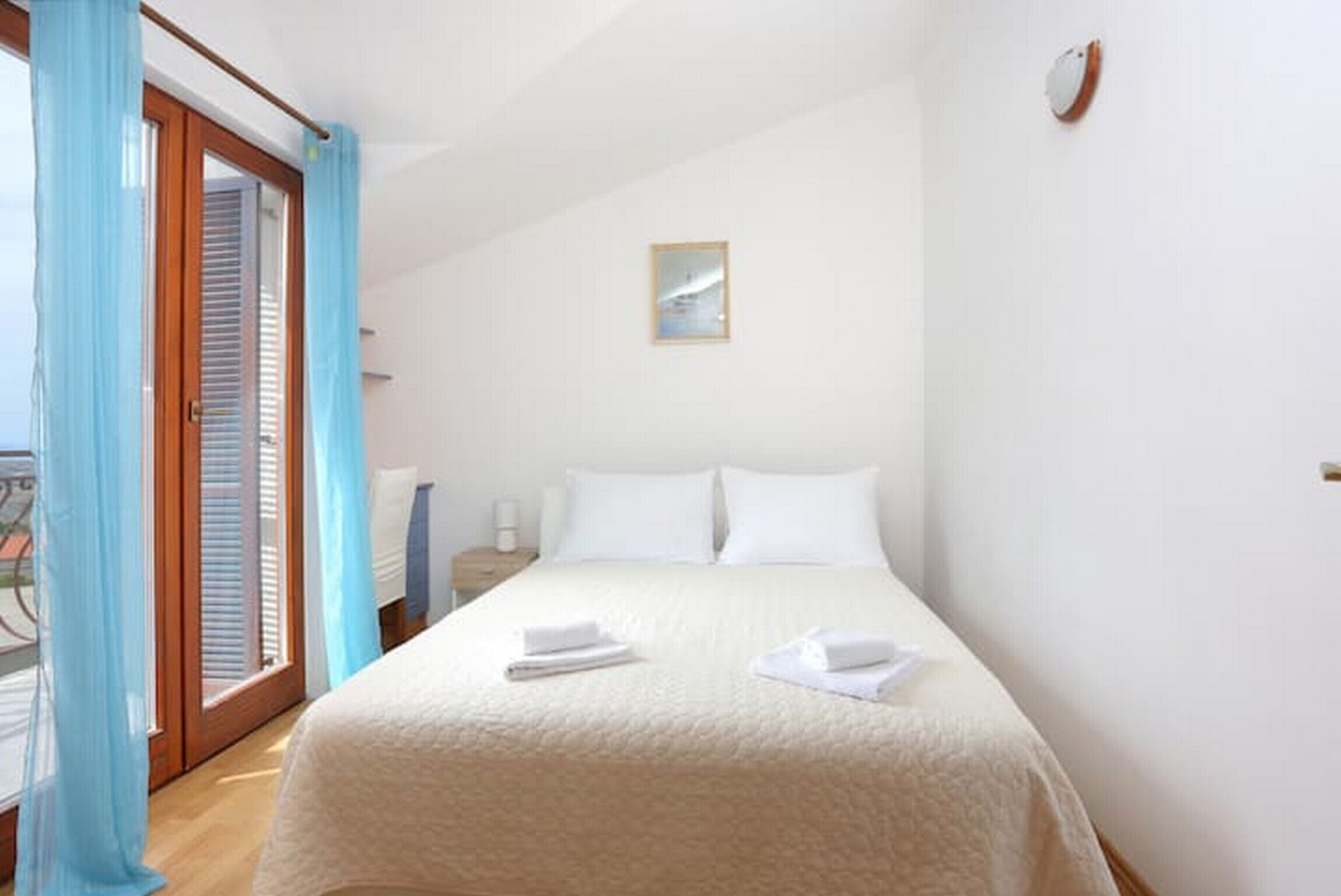 Une chambre d’hôtel avec un lit, une table de chevet, une fenêtre avec des rideaux et un luminaire fixé au mur.