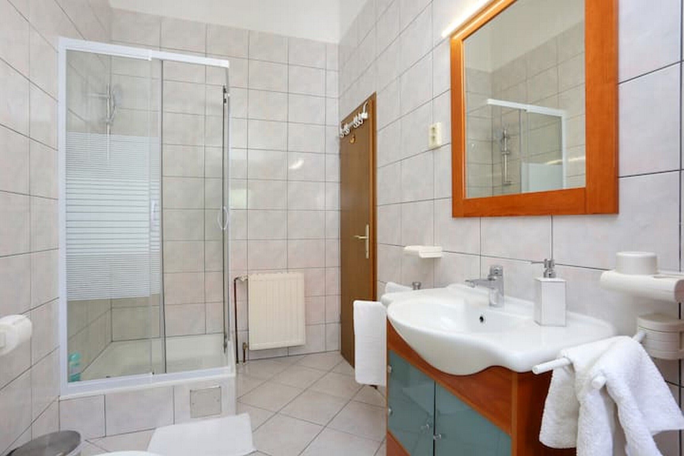 A modern bathroom with a glass-enclosed shower, a sink with a wooden vanity, and a large mirror.