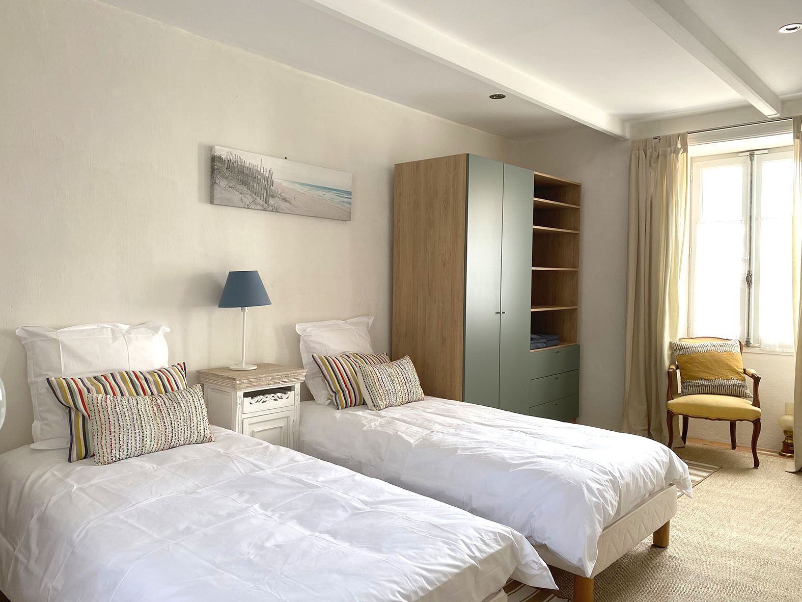 A hotel room with two beds, a nightstand, a lamp, a chair, and a wardrobe.