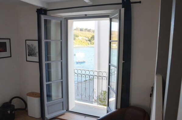 Una habitación con puerta de cristal corredera que da a un balcón con vista a una masa de agua y colinas.