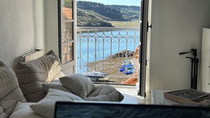 Ein Zimmer mit Blick auf ein Gewässer, ein Balkon mit Geländer und ein Stativ auf dem Boden.