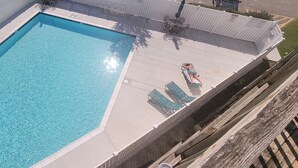 A rectangular pool with clear blue water, surrounded by a white deck and a wooden fence. There are lounge chairs and a table on the deck. - 2-bedroom condo with an outdoor pool located uptown on the bayside in a peaceful, family-friendly neighborhood! (OCEAN CITY)