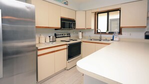 A modern kitchen with stainless steel appliances, wooden cabinets, and a large window. - 2-bedroom condo with an outdoor pool located uptown on the bayside in a peaceful, family-friendly neighborhood! (OCEAN CITY)