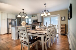A modern kitchen with white cabinetry, stainless steel appliances, and a dining area with a wooden table and white chairs. - Welcome to Anchors Away (South Haven)