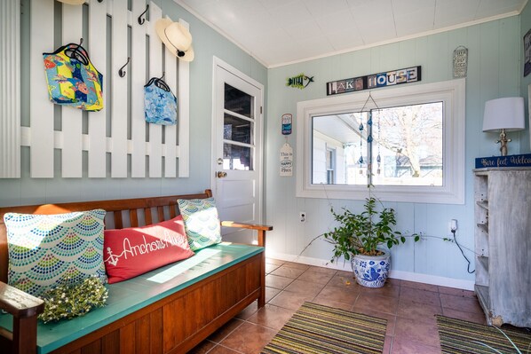 A cozy entryway with a wooden bench, colorful cushions, a potted plant, and nautical-themed wall decorations.