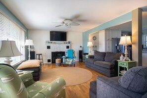 A living room with a fireplace, a ceiling fan, and a dining area with a table and chairs. - Welcome to Anchors Away (South Haven)