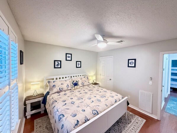 Une chambre à coucher avec un lit, une table de chevet, un ventilateur de plafond et des tableaux encadrés accrochés au mur.