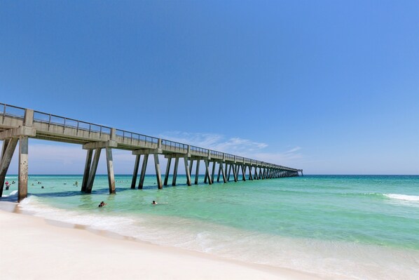 Un muelle que se adentra en el océano, con agua azul cristalina y una playa de arena.
