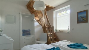 A bedroom with two beds, a wooden staircase, a white dresser, and a window with blinds. - Vacation home under thatch on Usedom for 6 people with sauna and wood-burning stove, wall box. (Zirchow)