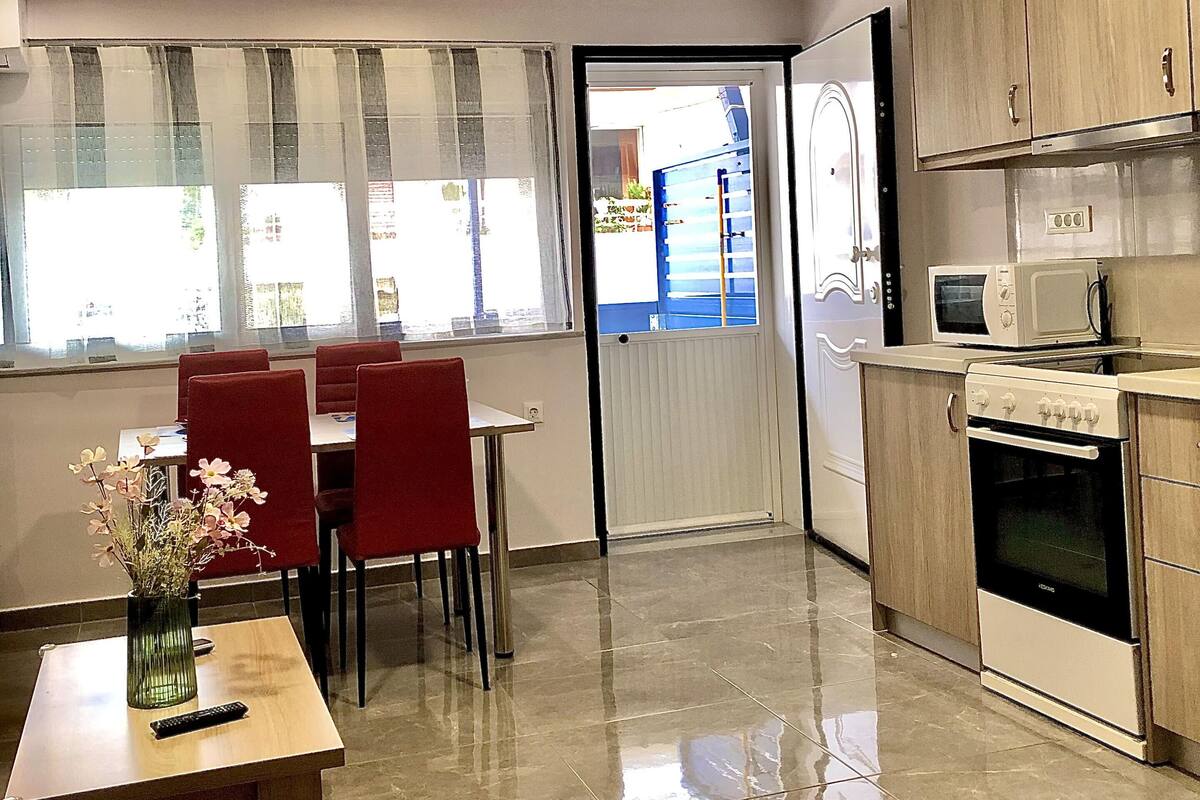 Eine moderne Küche mit Mikrowelle, Backofen und Holzschränken. Es gibt eine Essecke mit roten Stühlen und einem Tisch, und ein Fenster mit Vorhängen.