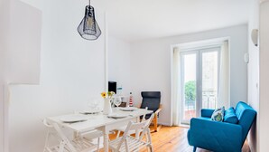 A dining area with a white table and chairs, a blue sofa, and a view of the outdoors through a glass door. - 2BR at Chiado Historical Heart of Lisbon (Lisbon)