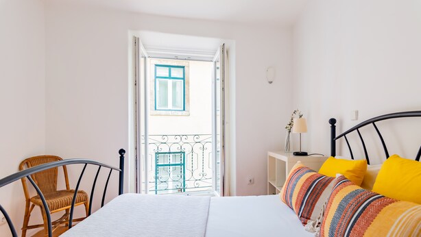 A bedroom with a bed, a chair, a nightstand, and a view of the outside balcony. - 2BR at Chiado Historical Heart of Lisbon (Lisbon)
