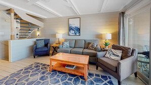 Ein modernes Wohnzimmer mit Sofa, Sessel, Couchtisch und einer Treppe zu einer oberen Etage.