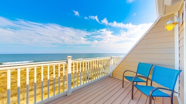 Eine Holzterrasse mit weißer Reling, die auf einen Strand blickt.