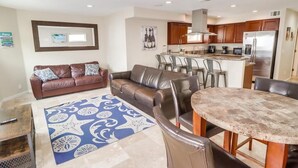 A modern living room with a brown leather sofa, a coffee table, and a patterned rug. - Jamaica Palms & Penthouse, Sleeps 22 (San Diego)