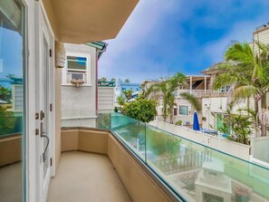 Un balcón con barandilla de vidrio que da a una zona residencial con palmeras y casas.