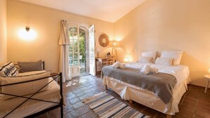 A bedroom with a bed, a desk, a chair, a sofa, and a door leading to a balcony.