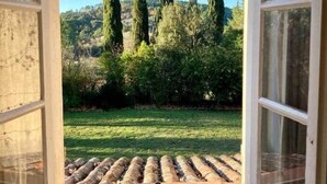 An open window with a view of a grassy area and tall trees.