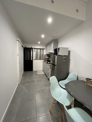 Une cuisine moderne avec des carreaux gris, un coin repas avec une table et des chaises, et une porte coulissante donnant sur une autre pièce.