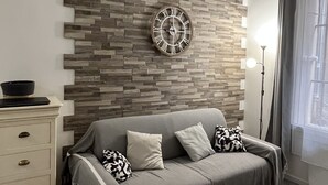 A modern living room with a grey sofa, a decorative clock, a white dresser, and a small round table. - TYPE2, a rare 4-person gem, ideally renovated (La Ciotat)