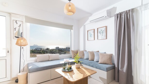 Una sala de estar moderna con un ventanal grande, un sofá, una mesa de centro de madera y vistas a la ciudad.