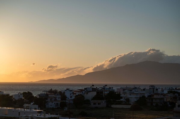 A coastal town at sunset with buildings and a mountain in the background.