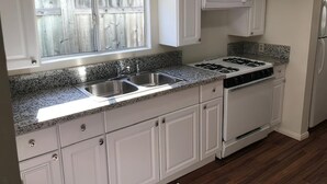 Una cocina con armarios blancos, un lavamanos doble, una estufa y un microondas.