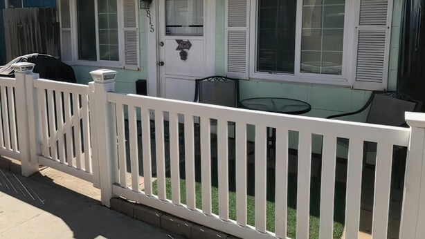 Una casa de un piso con valla de piquete blanca, una puerta principal y un pequeño patio con mesa y sillas.