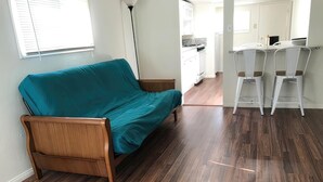 Una habitación con piso de madera, un sofá color turquesa y una kitchenette al fondo.