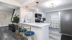 A modern kitchen with a central island, bar stools, and a refrigerator. - 1 Block to Allianz Field • Sleeps 8+ • Patio & Parking (Saint Paul)