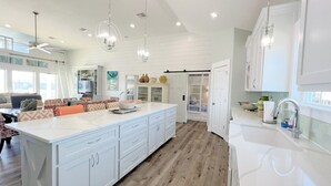 A spacious kitchen with a large island, white cabinetry, and a wooden floor. - Hooked On A Feeling 3 Bedroom Home by RedAwning (Port Bolivar)
