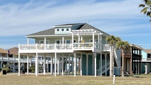 A two-story beachfront house with a balcony, a covered porch, and a staircase leading to the upper level. - Hooked On A Feeling 3 Bedroom Home by RedAwning (Port Bolivar)