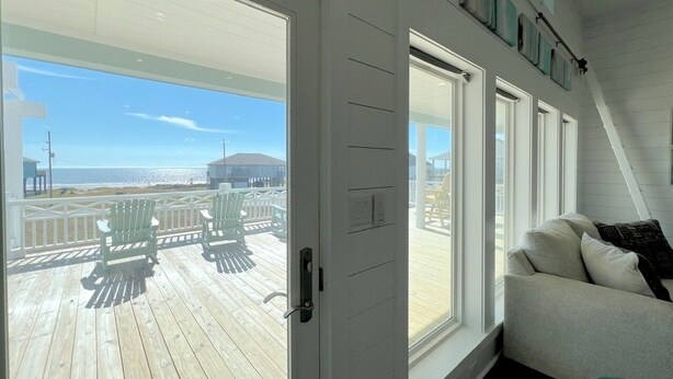 A room with a large window, a white door, and a view of a wooden deck with chairs. - Hooked On A Feeling 3 Bedroom Home by RedAwning (Port Bolivar)