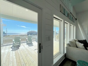 A room with a large window, a white door, and a view of a wooden deck with chairs. - Hooked On A Feeling 3 Bedroom Home by RedAwning (Port Bolivar)