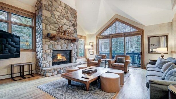 Amplia sala de estar con chimenea de piedra, asientos confortables y ventanas grandes con vistas al exterior.