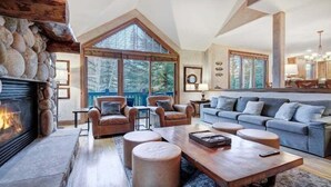 Amplia sala de estar con chimenea de piedra, sillones de cuero, un sofá azul y una mesa de centro de madera.