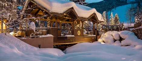 A snow-covered wooden structure with a sign indicating it's a visitor's area, surrounded by snow and trees.