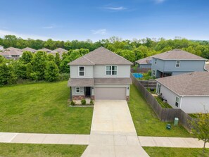 A two-story house with a front yard, a garage, and a swimming pool in the background.