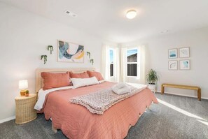 A bedroom with a bed, a bedside lamp, a small plant, and a picture on the wall.