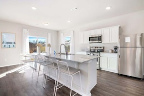A modern kitchen with white cabinetry, stainless steel appliances, and a central island with bar stools.