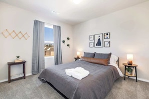 A bedroom with a bed, two bedside tables, a window with curtains, and wall art.