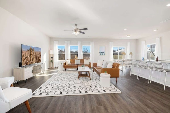 A spacious living room with a large TV, a ceiling fan, and a dining area with a bar.