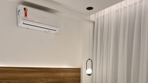 Une chambre d’hôtel avec une tête de lit en bois, du linge de lit blanc, un lit bien fait avec des serviettes, un appareil de climatisation et un luminaire suspendu.