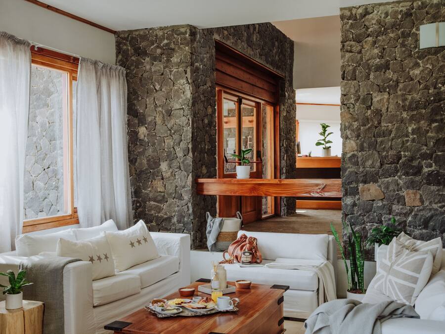 Un vaste espace de vie agrémenté d’un mur en pierre, de meubles blancs et d’une table basse en bois sur laquelle sont disposés des éléments pour le petit-déjeuner.