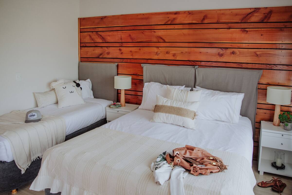 Une chambre d’hôtel avec deux lits, une tête de lit en bois, des tables de chevet avec des lampes et une petite table de nuit avec une plante.