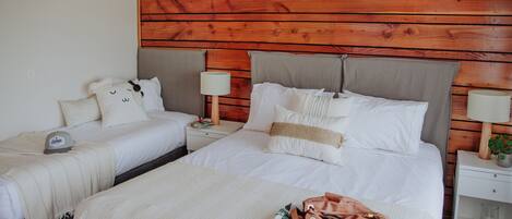 A hotel room with two beds, wooden headboard, bedside tables with lamps, and a nightstand with a plant.