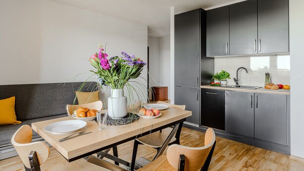 A modern kitchen with dark cabinets, a wooden dining table, and a sofa with cushions. - P&O Apartments Ostrobramska (Warsaw)