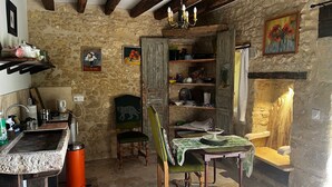 Una cocina rústica con paredes de piedra, vigas de madera, una mesa de comedor con mantel verde y una silla con motivos de pavo real.